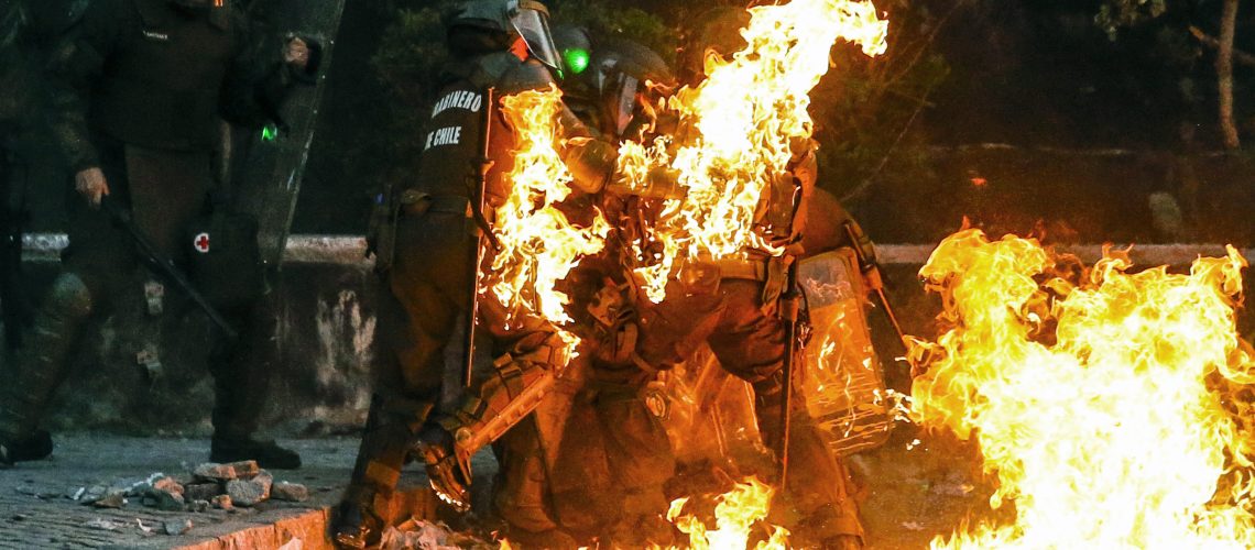 Riot police are reached by a petrol bomb during clashes with demonstrators protesting against the government in Santiago on November 22, 2019. - Chilean President Sebastian Pinera said on Thursday that police may have broken protocols in responding to a month of protests, and prosecutors will investigate whether they violated human rights. (Photo by JAVIER TORRES / AFP)